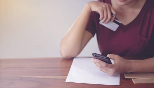 A person filling out a credit card debt forgiveness application form, with a calculator and financial documents on the table.