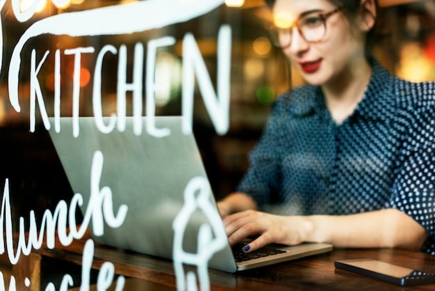 A person working on a laptop in a modern cafe. The screen displays a profile page with professional headshot, skills, and experience details, illustrating the digital aspect of personal branding.