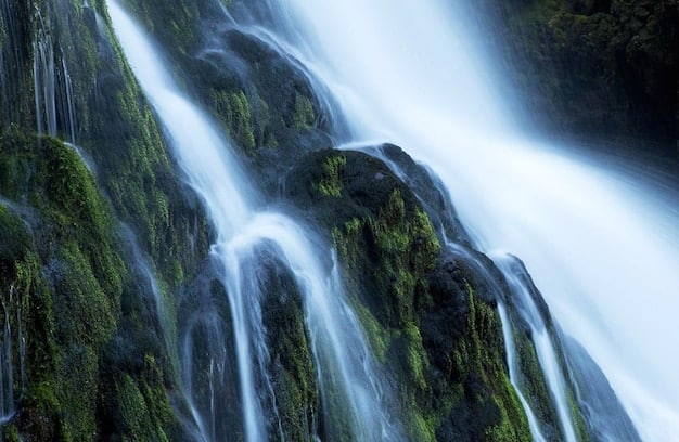 A long exposure shot of a waterfall in the Northeast, showing the water flowing smoothly over the rocks, surrounded by vibrant autumn foliage. The scene is peaceful and serene, with the sound of the water creating a calming effect.