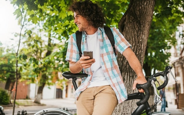A digital nomad using a smartphone for navigation while riding a bicycle through a scenic urban park. The background shows a sunny day and various people enjoying the park.
