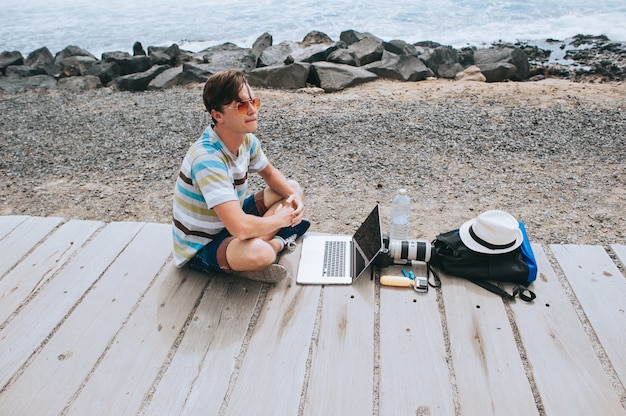 A digital nomad working on a laptop while sitting on a beach, with the ocean and sunset in the background. The scene should convey a sense of relaxation, freedom, and productivity in a beautiful, natural setting.